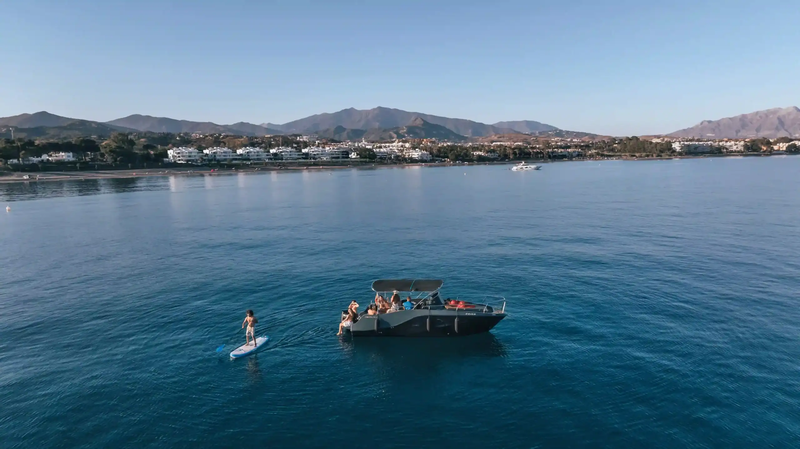A boat at anchor and a guest enjoying a stand-up paddleboard